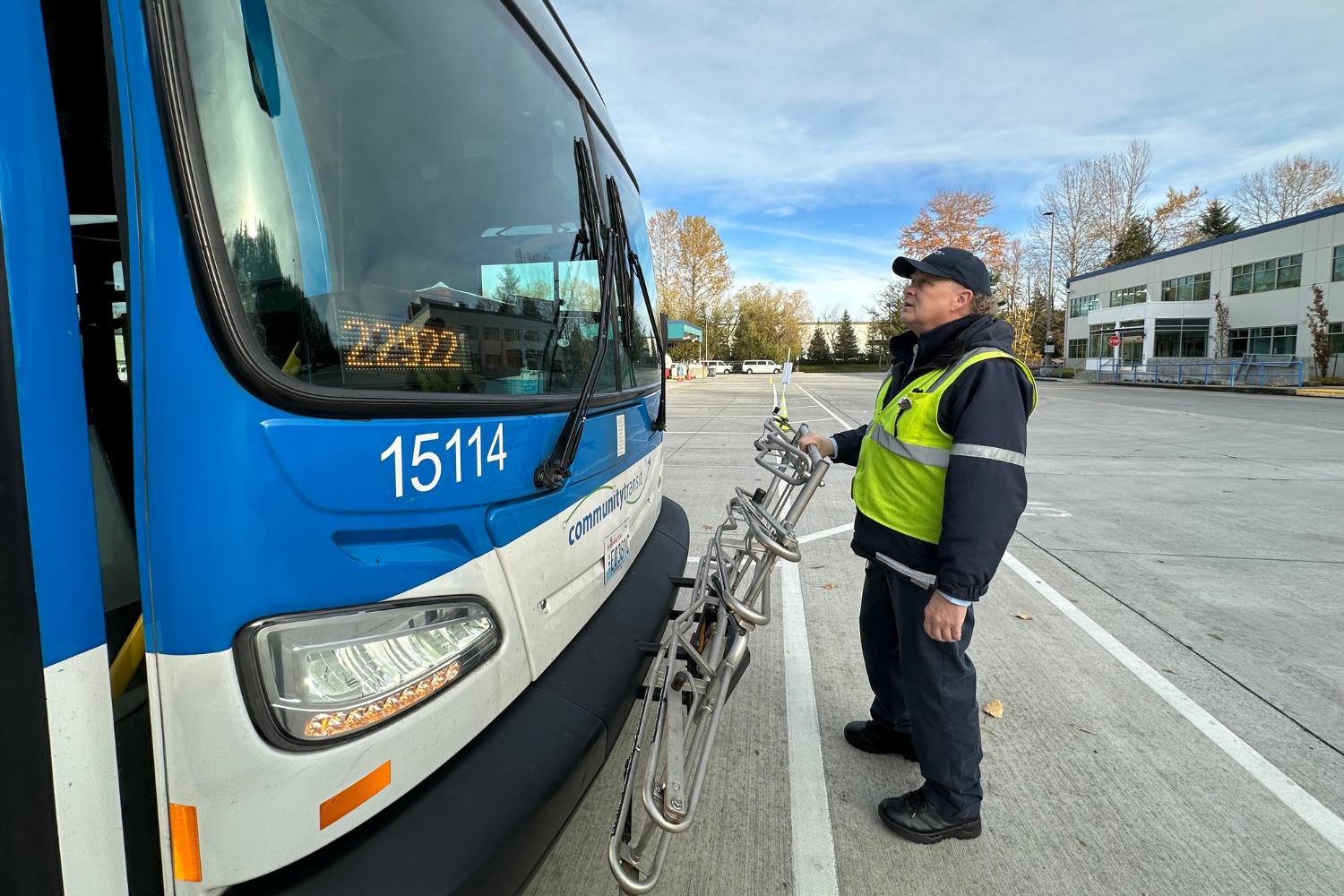 A Community Transit driver standing in front of a bus inspecting a bike rack. 