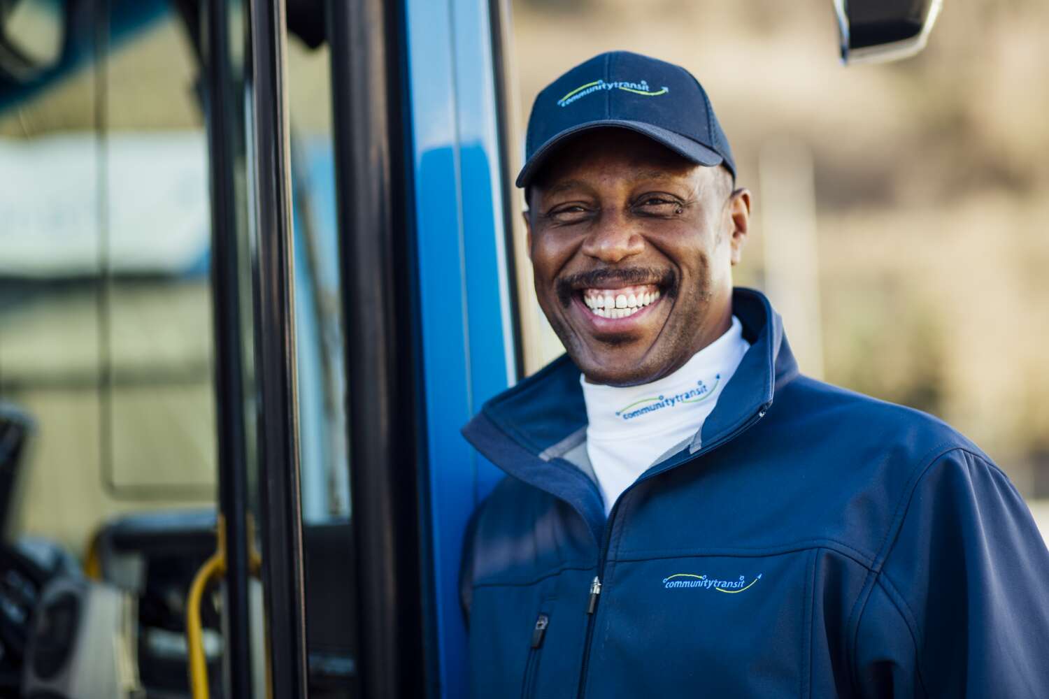 A smiling bus driver stands in front of a CT bus.