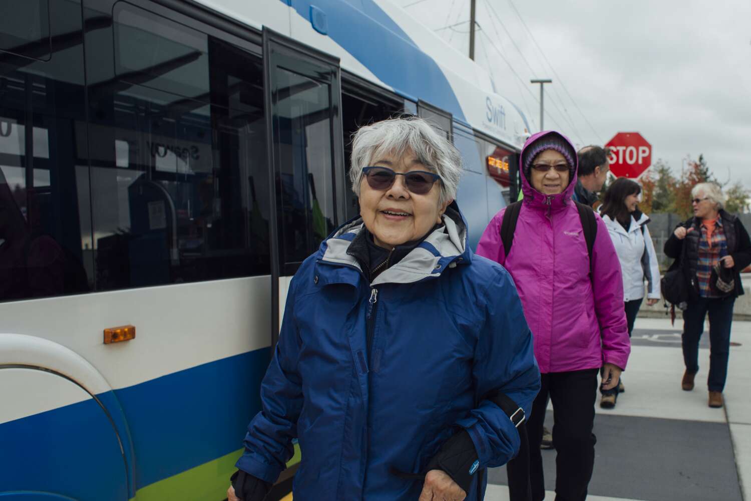 An older adult rider smiles in front of a Community Transit bus. 