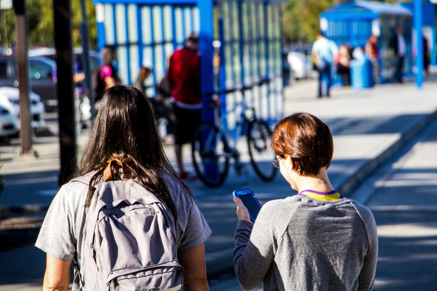 Two people walking to Mariner Park & Ride on a sunny day. One of them is looking at their cell phone.