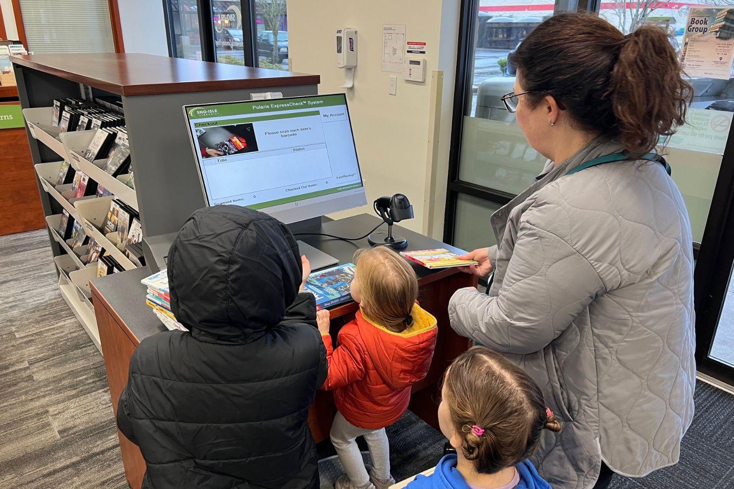 Three children and an adult woman check out books at the library. 