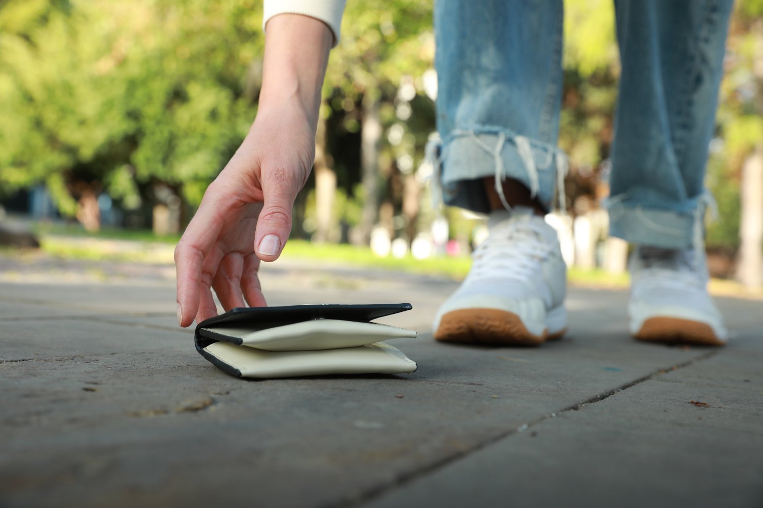 A person reaching down to pick up a wallet that was dropped on the ground.