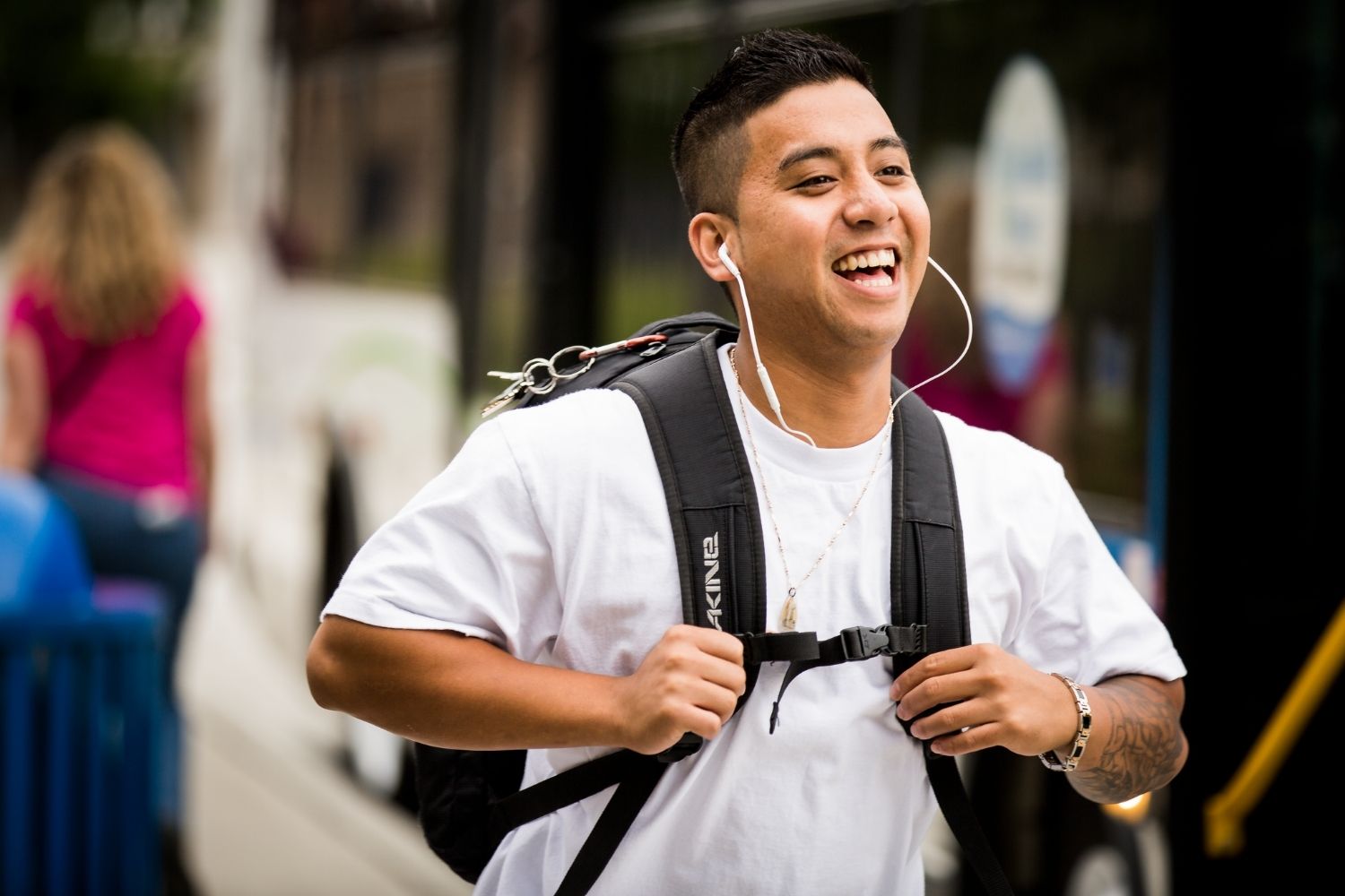A man standing in front of a bus wearing a backpack and headphones.