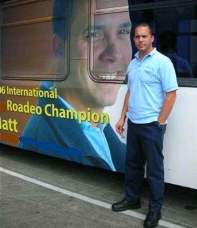 A man standing in front of a bus that is wrapped with his face on it. 