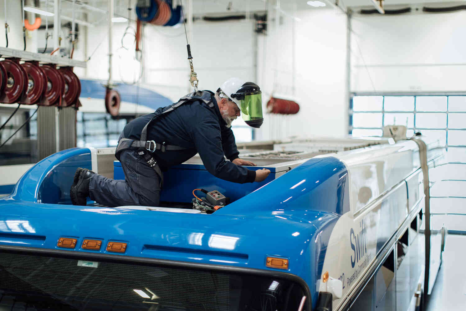 Mechanic Recruitment 072225-1-Website Standard - MEDIUM Compression Quality-1500x1000 A picture of a mechanic working on top of a bus. The mechanic wears a harness and a hard card.