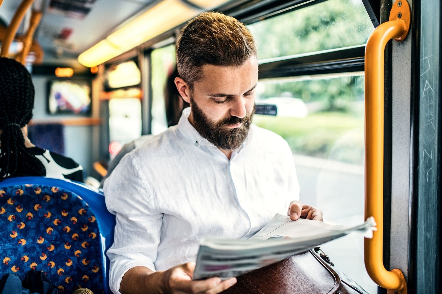 A man sitting on the bus and looking at a newspaper.