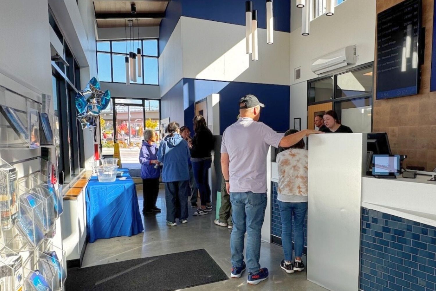 An image of people standing in front of the counter in the Ride Store. They are being helped by Ride Store employees behind the counter. In the foreground is a wall displaying pamphlets and flyers for people to take.