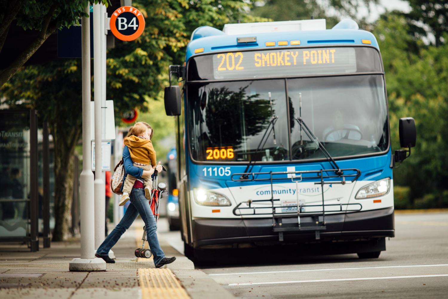 A woman crosses the street in front of a bus