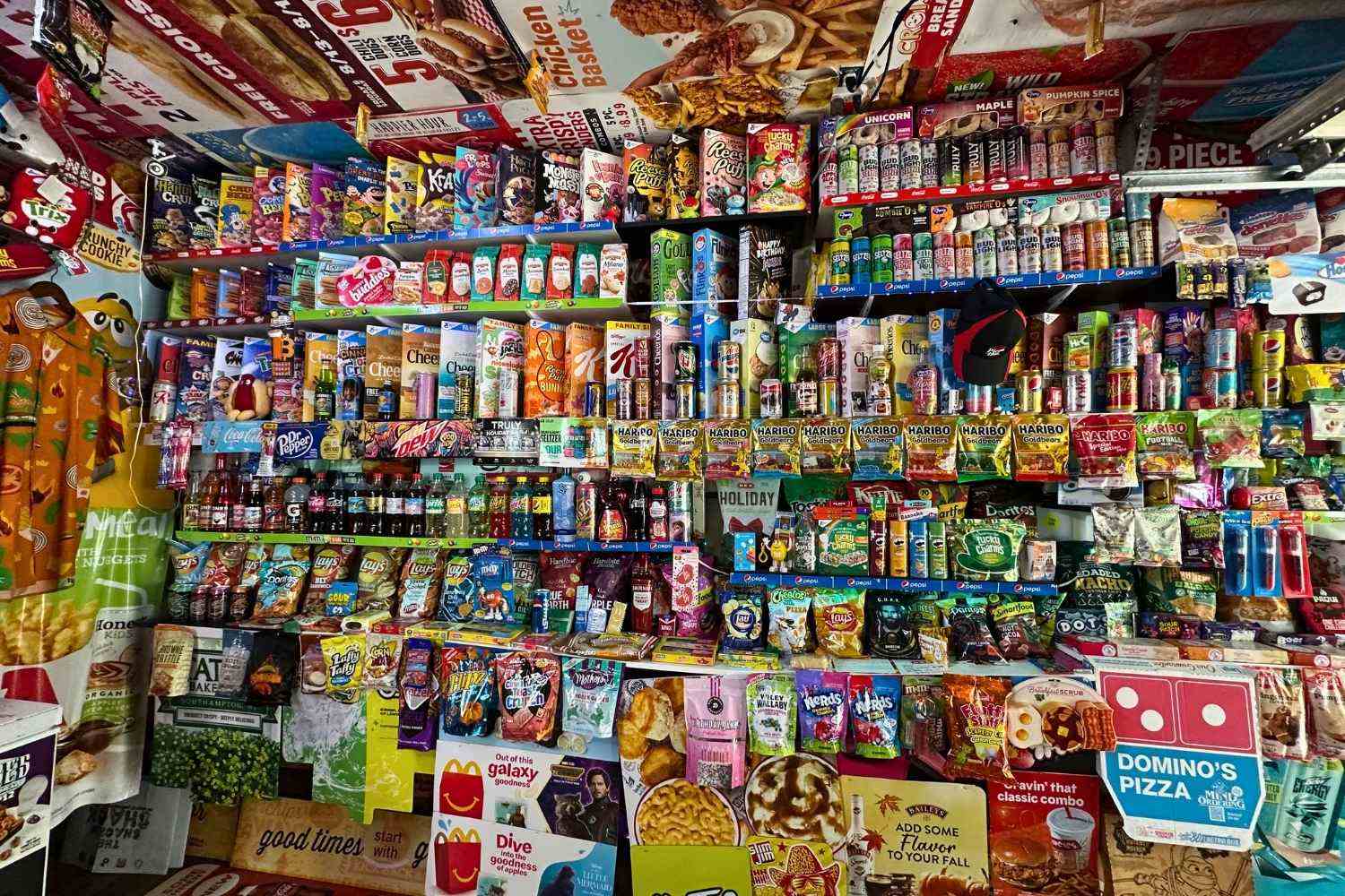 Wall filled with colorful snacks and drinks, including chips, candy, cereals, sodas, and branded packaging.