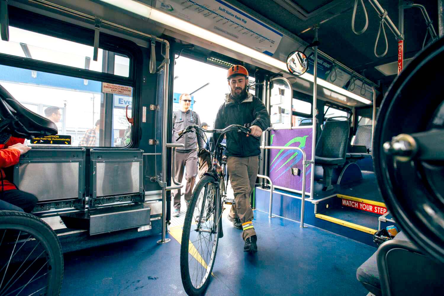 A man wearing a helmet walks his bicycle onto a bus while another person waits outside.