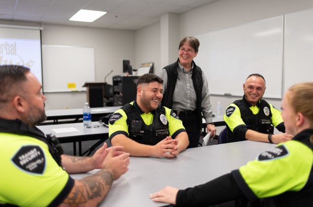 TSO Transit Security Officers in yellow uniforms sit around a table smiling and talking.