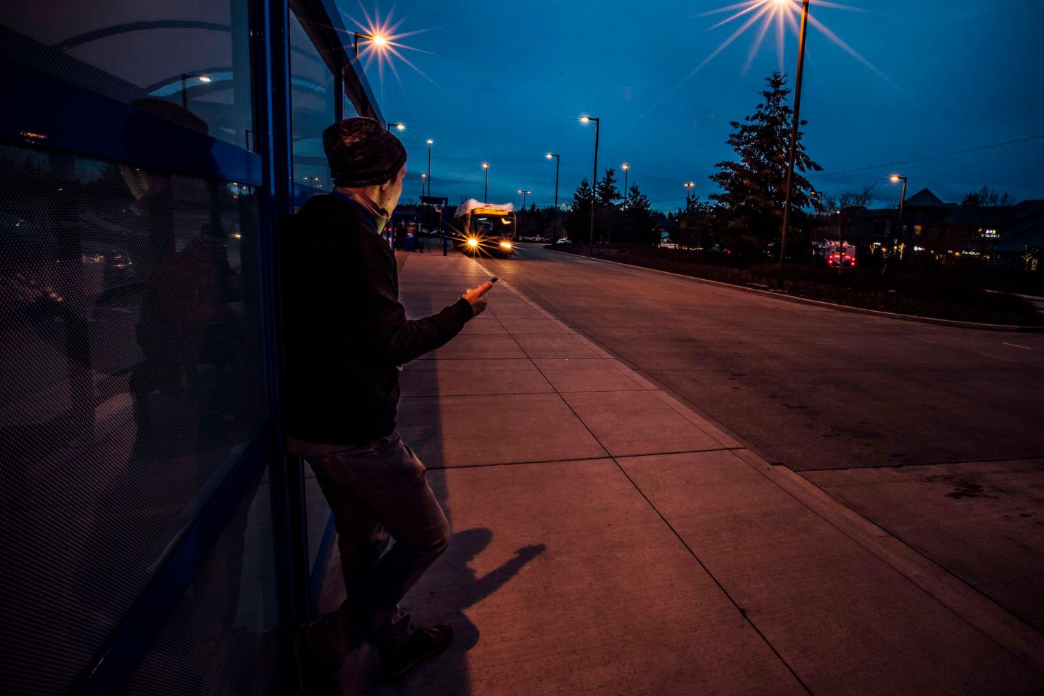 A man waits for a Community Transit bus at Mariner Park & Ride. It is a dark fall morning.