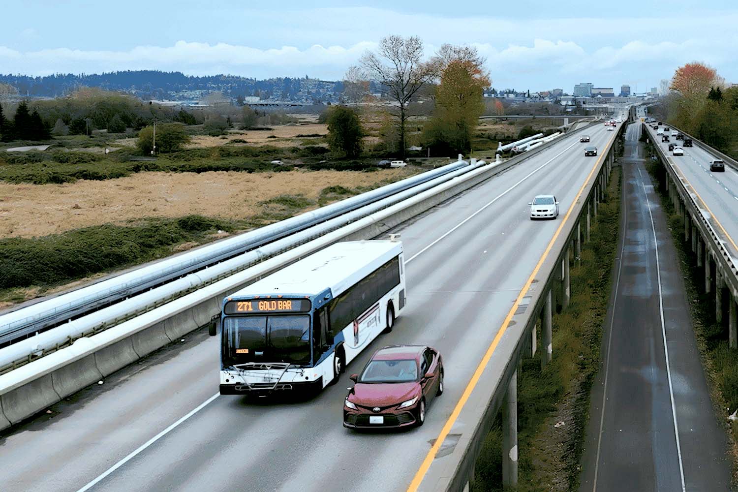 A Community Transit bus serving Route 271 travels eastbound on the trestle. A red car is on its right.