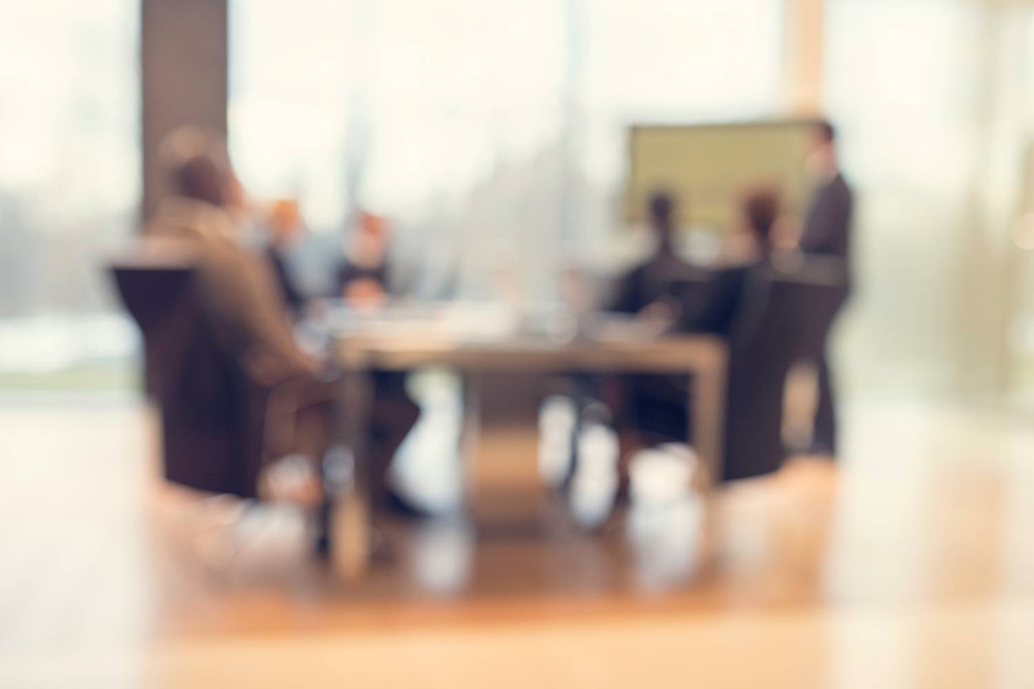 A stylized, blurred photo of a meeting of board members around a table