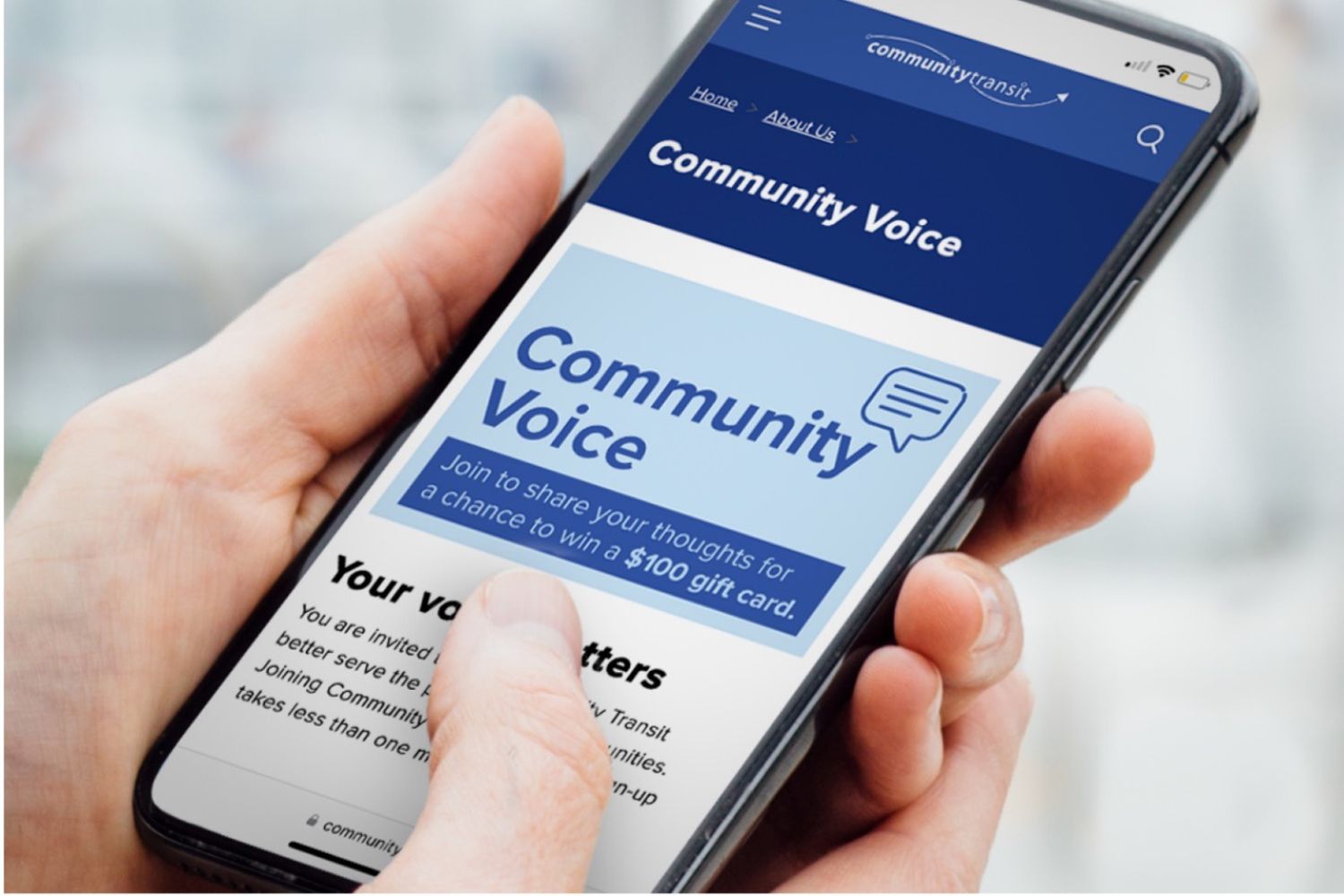 A man holds a mobile device, reading about how to participate in Community Voice