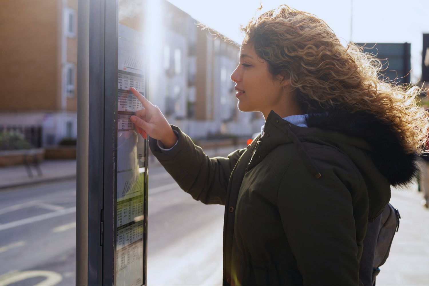 A young woman in a winter coat reviews a schedule at a bus stop