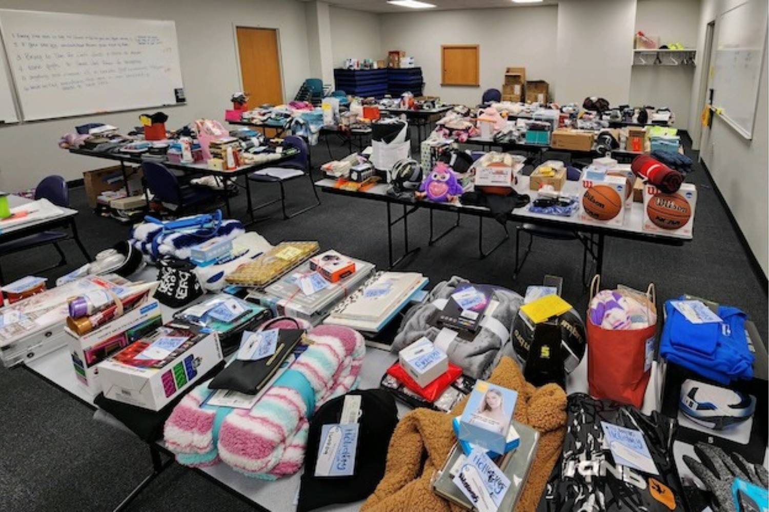 A roomful of long tables are filled with gifts and donations ready to be wrapped for holiday giving