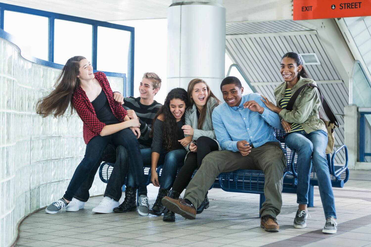 Happy teens attempt to fit on a bench at a transit center.