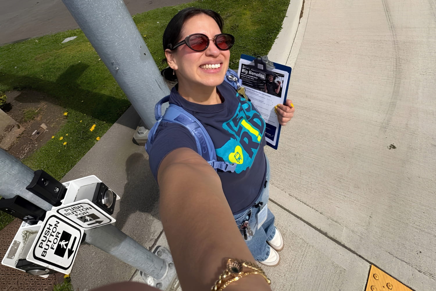 A young woman smiles for a selfie while waiting at an intersection.
