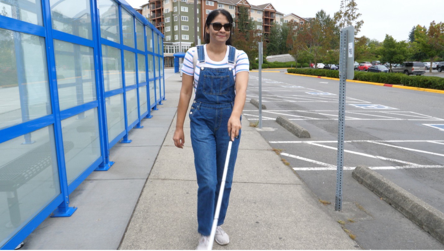 A vision impaired woman uses a mobility cane to make her way along bus shelters at Ash Way Park & Ride