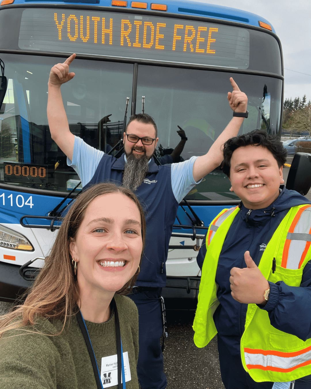 Natalie - Youth Ride Free Three smiling people pose in front of a Community Transit bus; one points enthusiastically at the illuminated “Youth Ride Free” sign while another gives a thumbs-up.