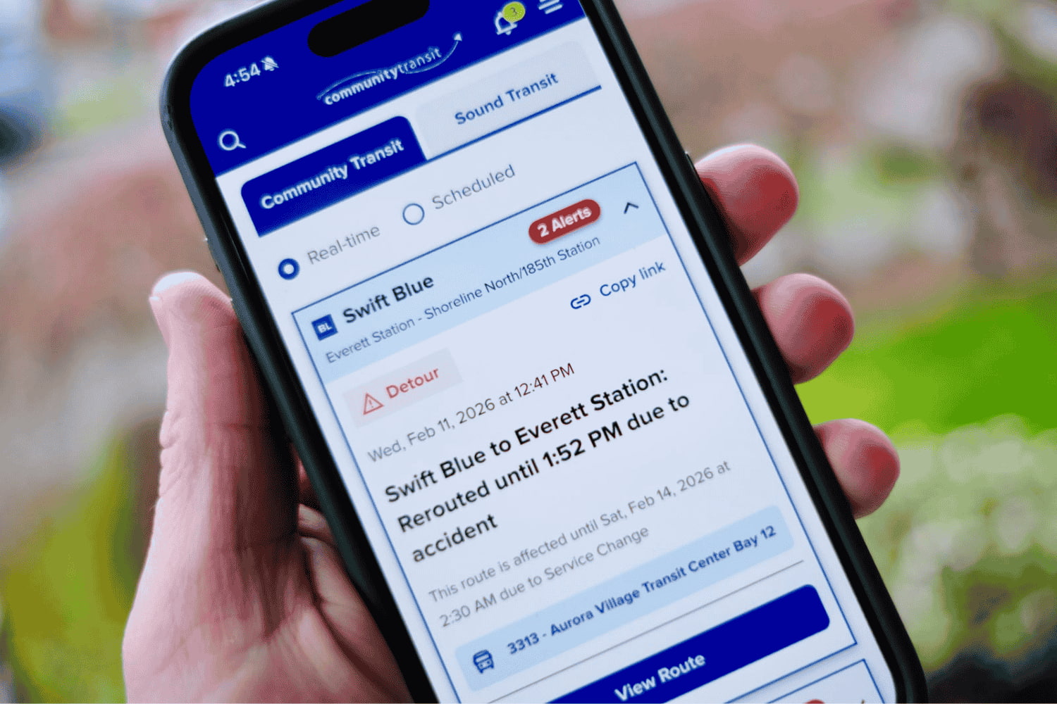 A hand holds a mobile phone displaying Community Transit's  improved rider alert layout