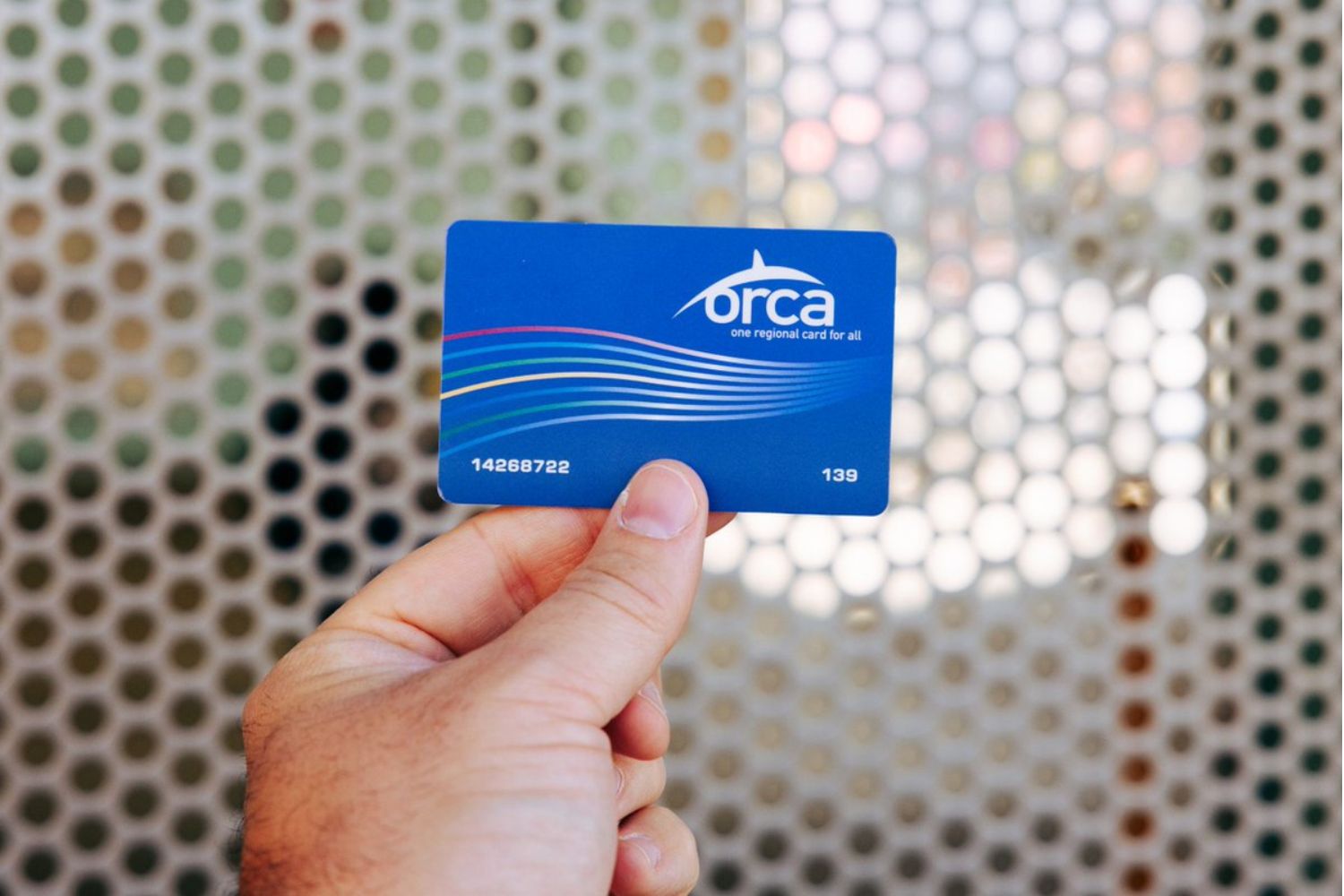 A man's hand holds a blue Classic ORCA Card.