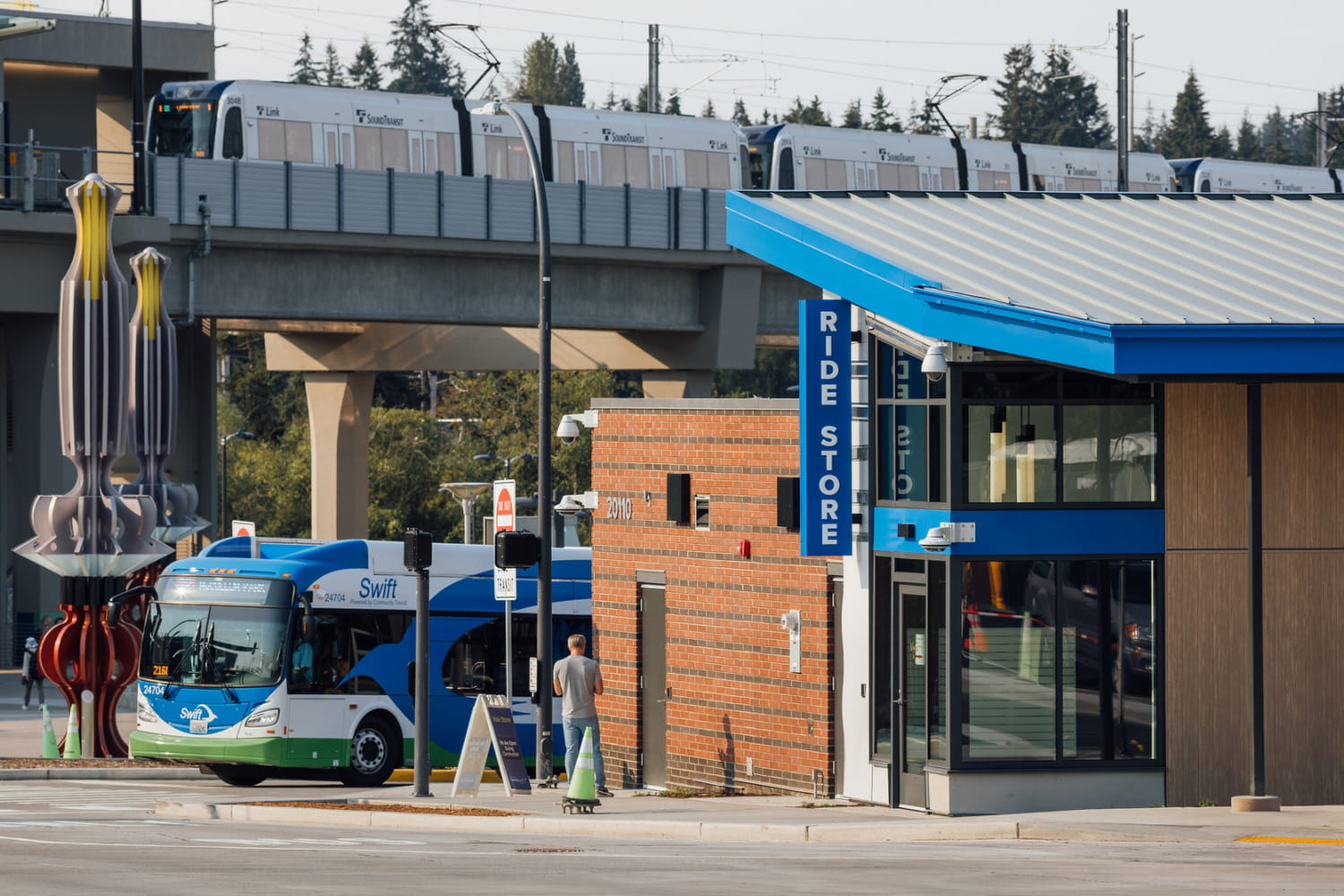 A Swift Bus and Light Rail train arrive at Lynnwood City Center. The Ride Store is on the right.