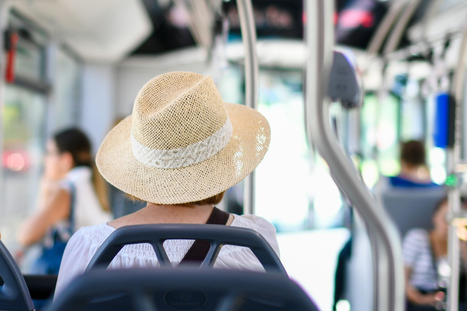 A woman wearing a summer straw hat sits on the bus.