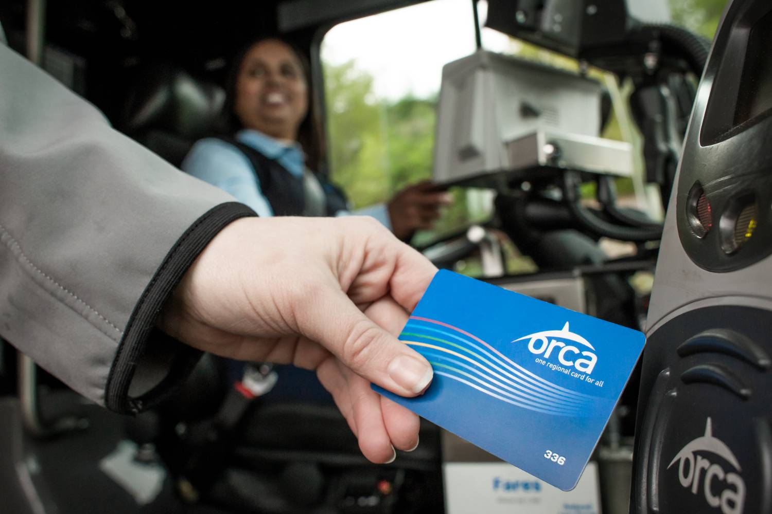 Woman's hand swipes ORCA card on scanner to pay fare as she boards CT bus