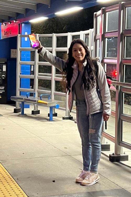 Young woman demonstrates how to use a mobile phone to signal a bus to stop