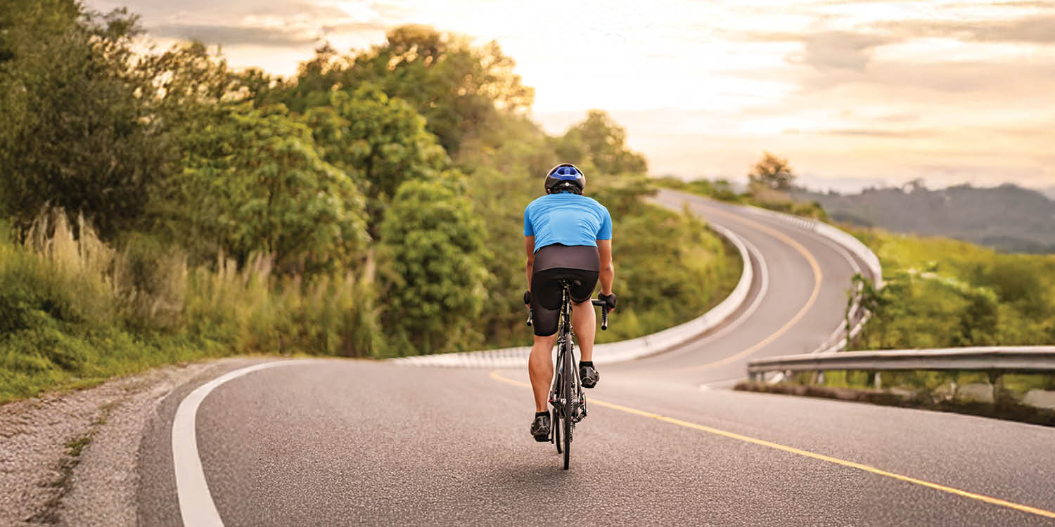 A biker is shown on a scenic Pacific Northwest road.