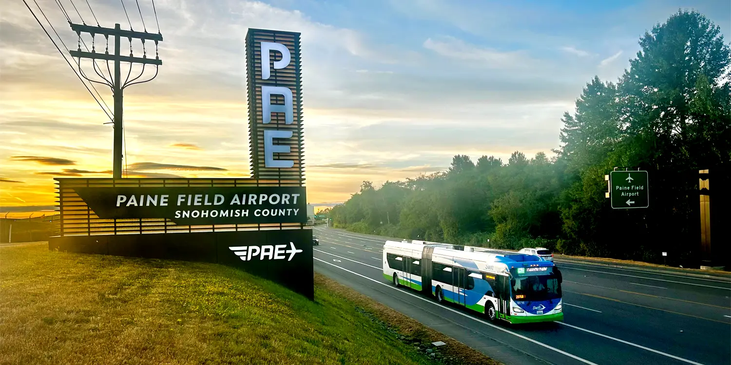 a Swift Green Line bus passing by the Paine Field Airport sign at sunrise