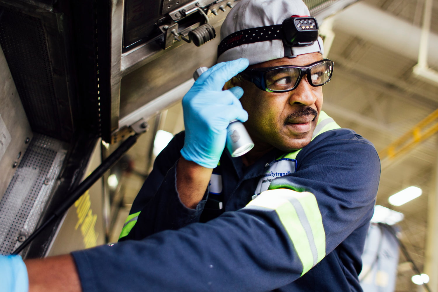 A mechanic works under the hood of Community Transit bus. He is wearing safety goggles and a headlamp.