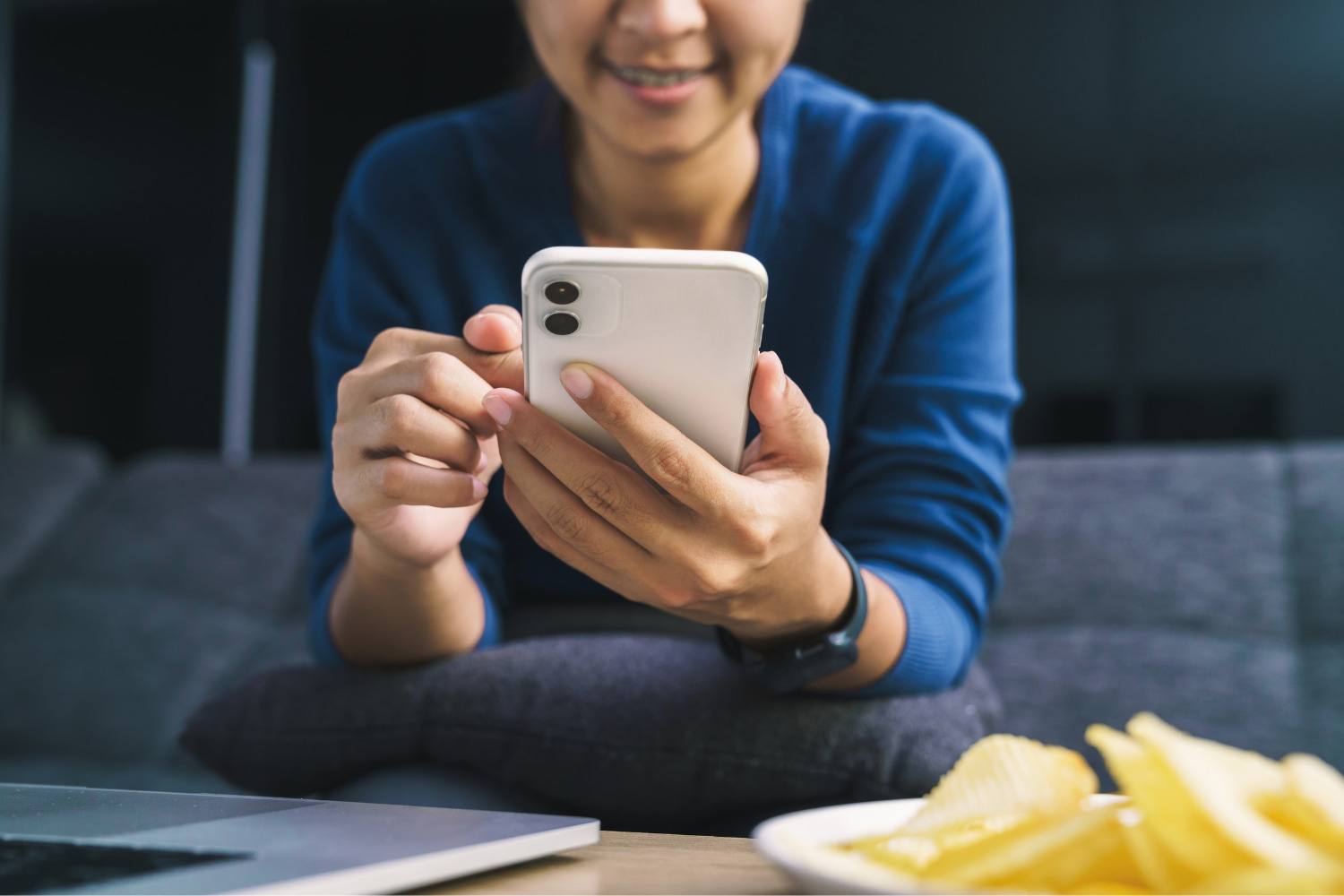 A woman wearing a blue sweater smiles as she looks at her mobile phone