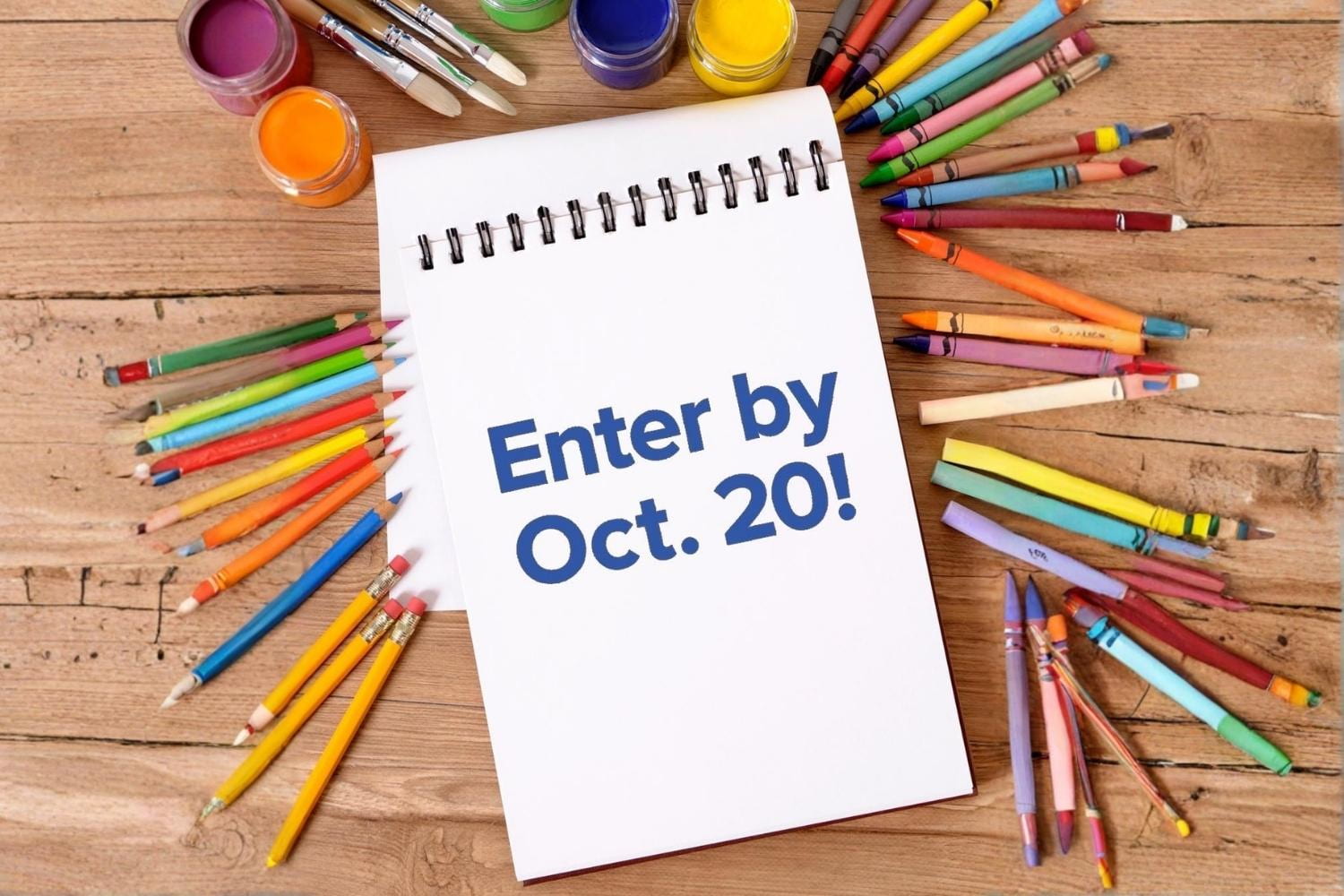 A notepad sits on a wooden table with art supplies.