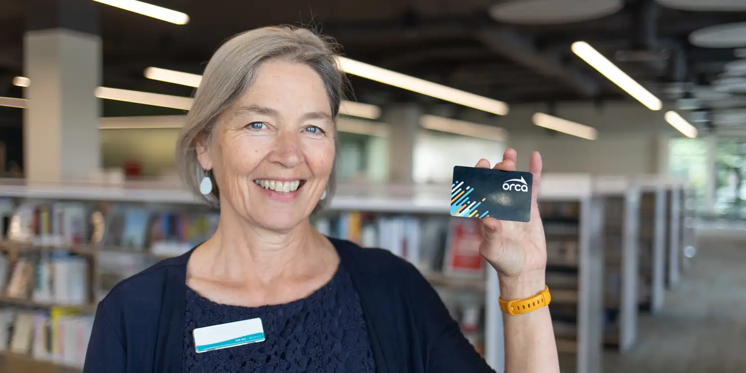 a librarian holding up an ORCA card and smiling at the camera