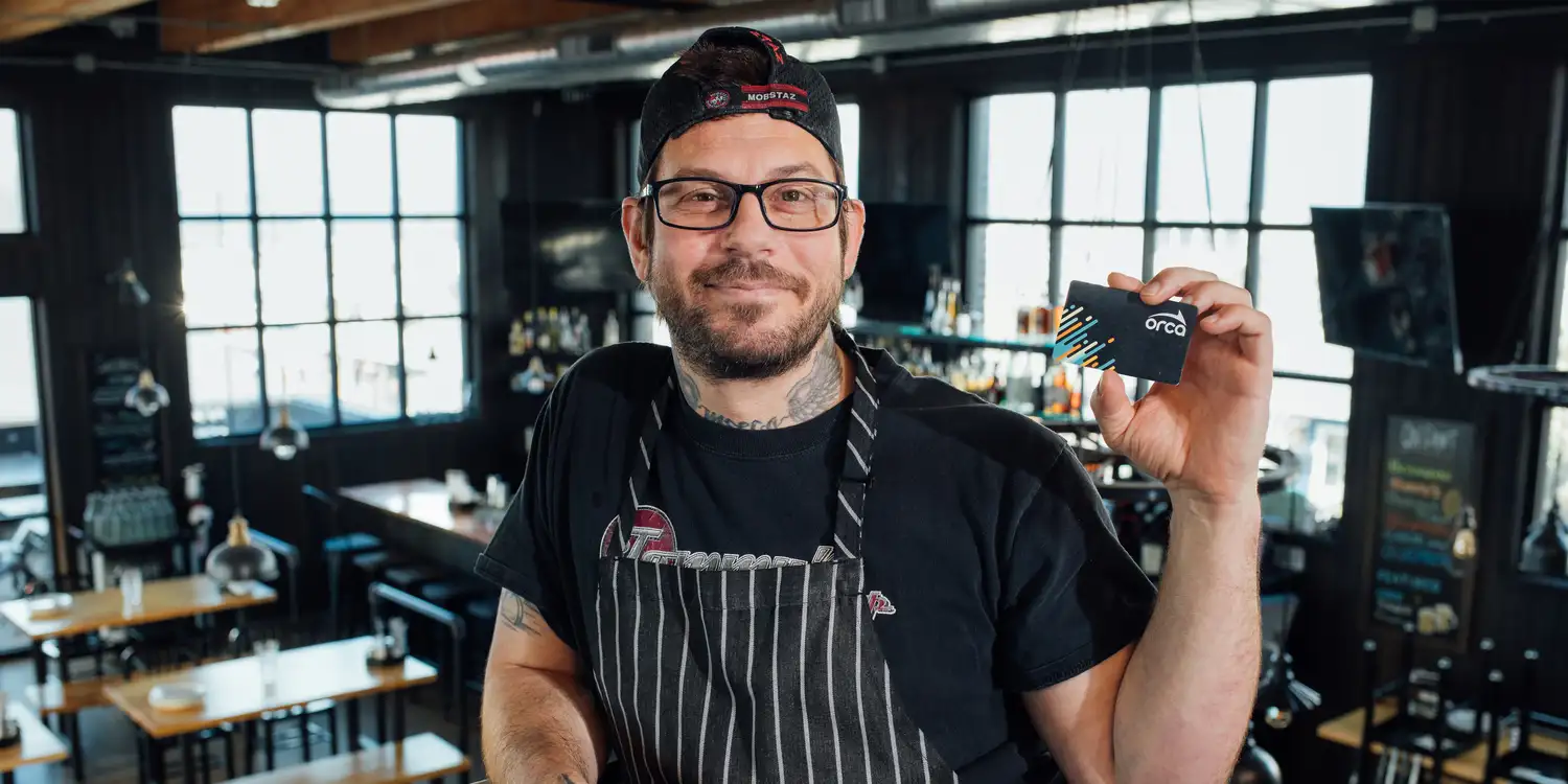 the owner of a small restaurant business holding up an ORCA card