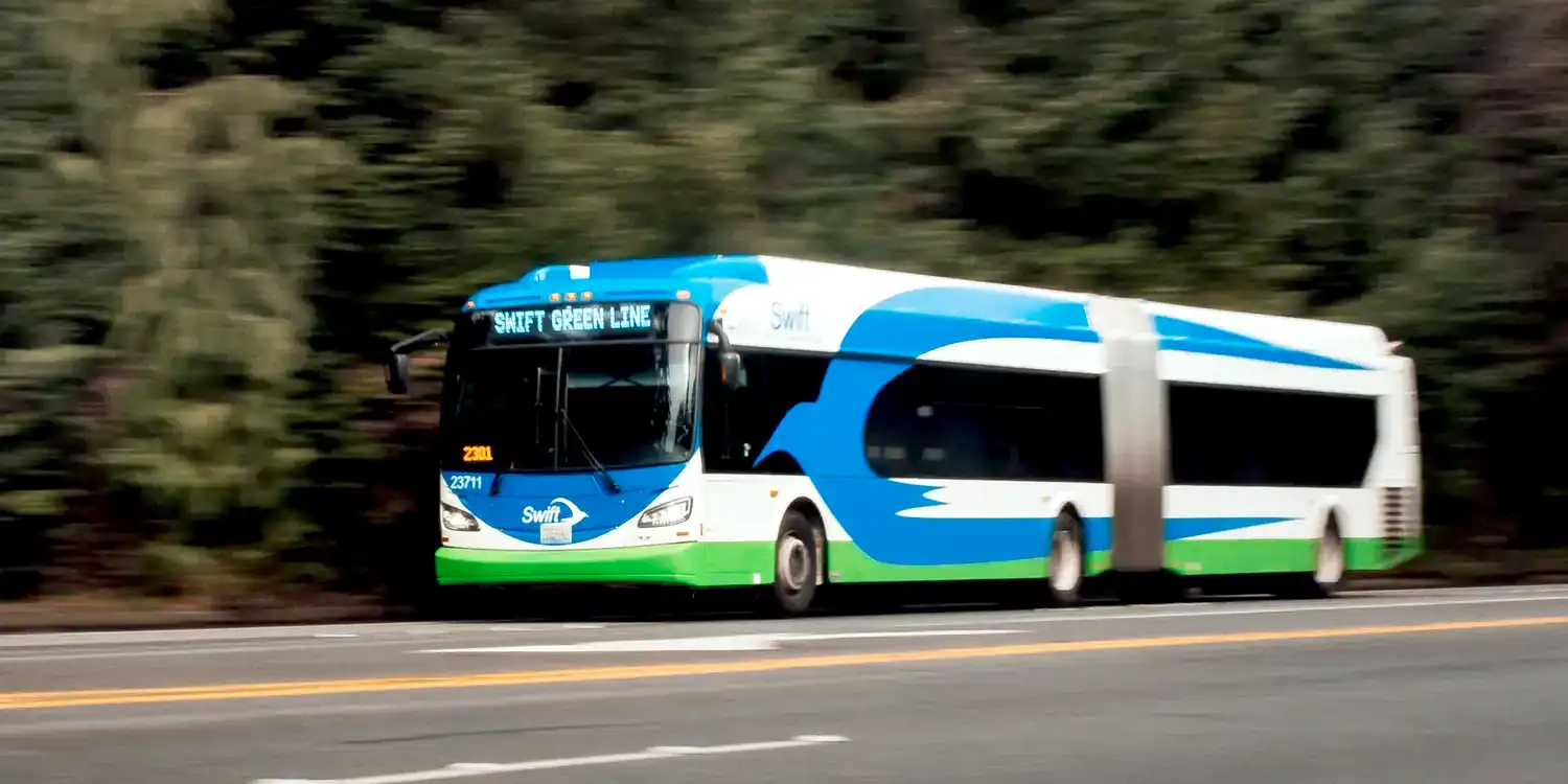a Swift rapid transit bus driving on a road lined by evergreen trees