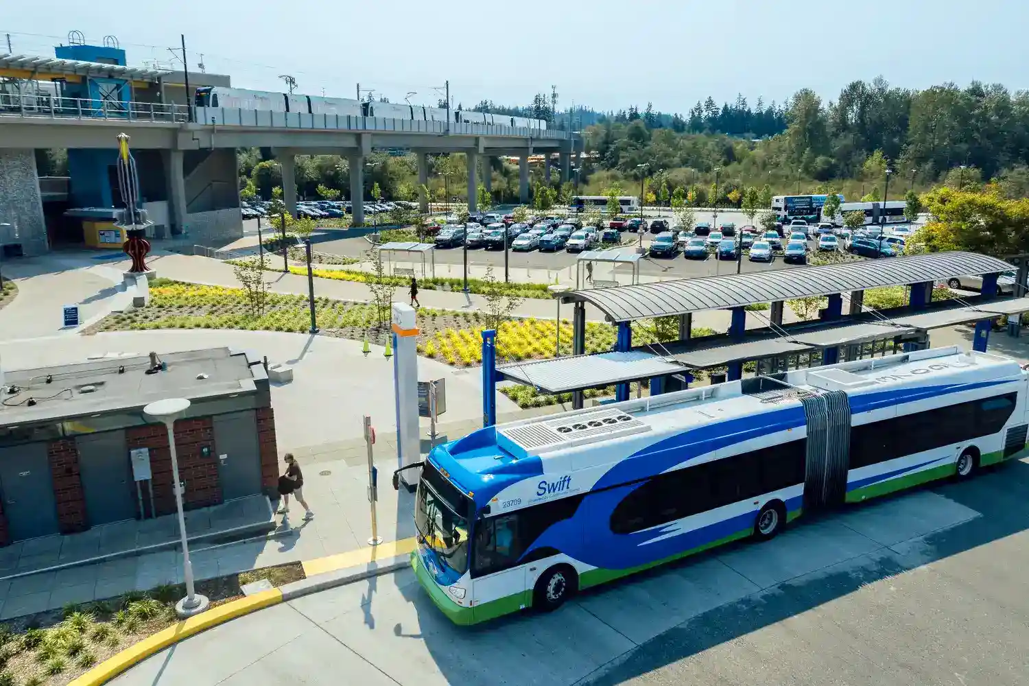 an aerial photo of a Swift bus at Lynnwood City Center station with a parking lot of cars and light rail train in the background