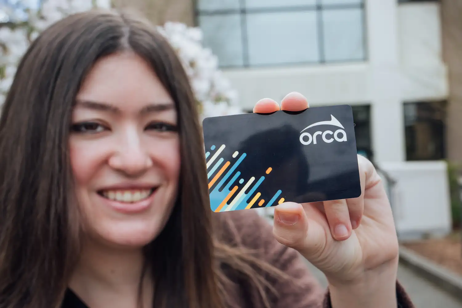 a woman smiling while holding up an ORCA card