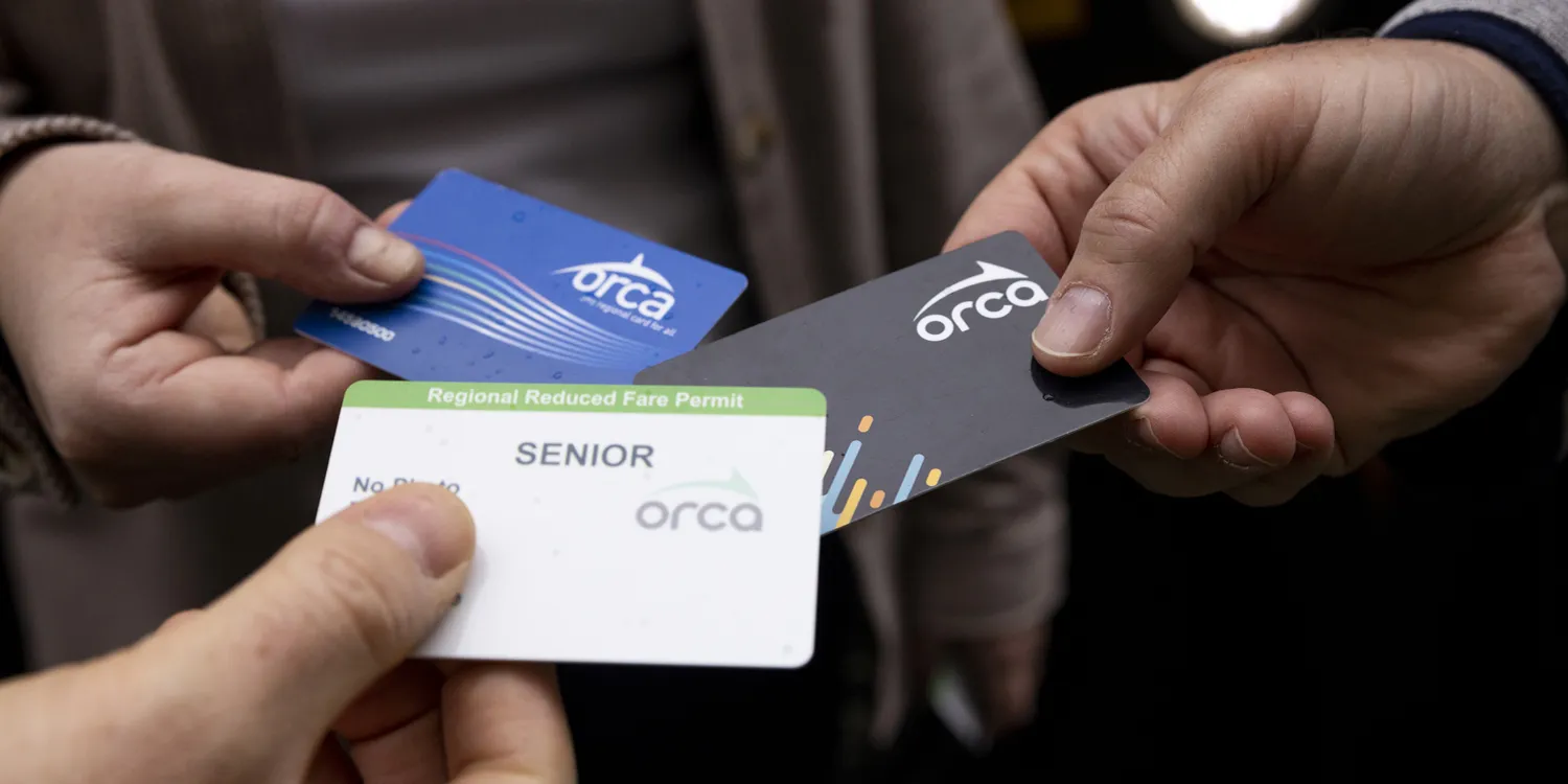 three riders holding three different ORCA cards in comparison