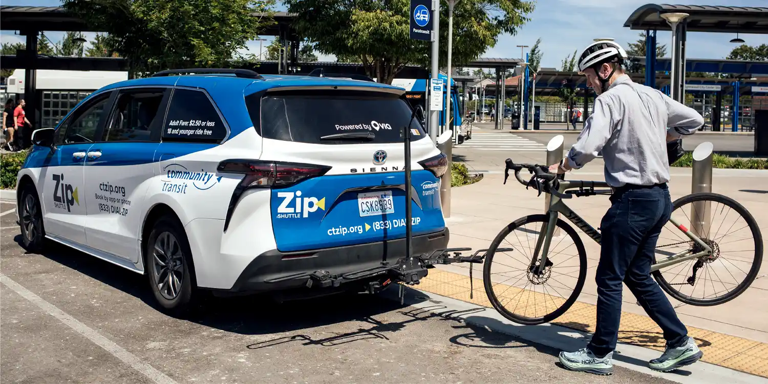 a rider loading their bicycle onto a Zip Shuttle van equipped with a bike rack