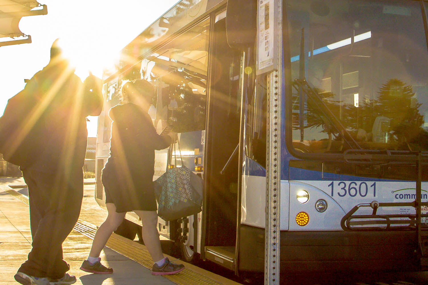 Riders boarding a bus with the sun setting behind them